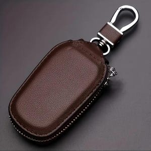 Puede incluir: Un llavero de cuero marr&oacute;n con una bolsa con cremallera y un gancho de metal plateado.