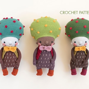 Puede incluir: Tres muñecos de crochet con forma de seta con caras sonrientes, cada uno con una pajarita y una mochila. Los muñecos tienen sombreros de seta de diferentes colores: turquesa con puntos rojos, verde con puntos amarillos y verde con puntos rojos. El texto "CROCHET PATTERN" está encima de los muñecos.