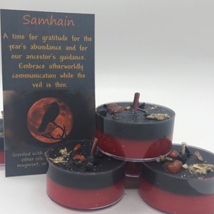 May include: Black and red tea light candles with decorative elements. A card with the word "Samhain" and text about gratitude and ancestor guidance is in the background. The candles are scented with mugwort and other oils.