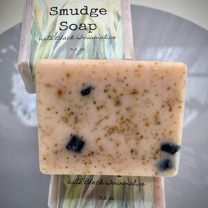 May include: A bar of pink soap with black tourmaline and herbs, labeled "Smudge Soap with Black Tourmaline 3.2 oz. Goat's milk and glycerin".