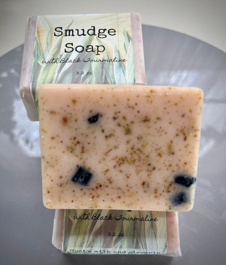 May include: A bar of pink soap with black tourmaline and herbs, labeled "Smudge Soap with Black Tourmaline 3.2 oz. Goat's milk and glycerin".