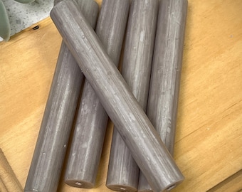 Pode incluir: Seis velas cinzas de forma cónica com um acabamento texturizado. As velas estão empilhadas sobre uma superfície de madeira.