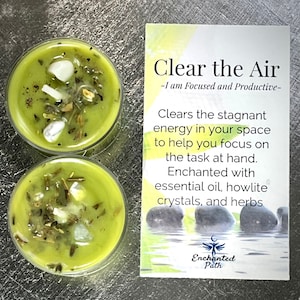 May include: Two green tea light candles with white crystals and herbs inside. The candles are labeled "Clear the Air - I am Focused and Productive - Clears the stagnant energy in your space to help you focus on the task at hand. Enchanted with essential oil, howlite crystals, and herbs. Enchanted Path"