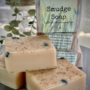 May include: Three bars of handmade soap with a light beige color and black flecks. The top bar has a label that reads "Smudge Soap with Black Tourmaline 3.2 oz."