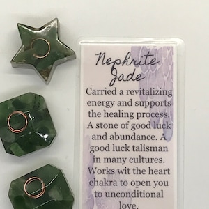 May include: Three green nephrite jade stones, each with a copper wire wrapped around it. The stones are shaped like a star, a square, and a rectangle. A card with the text "Nephrite Jade" and information about the stone's properties is in the background.