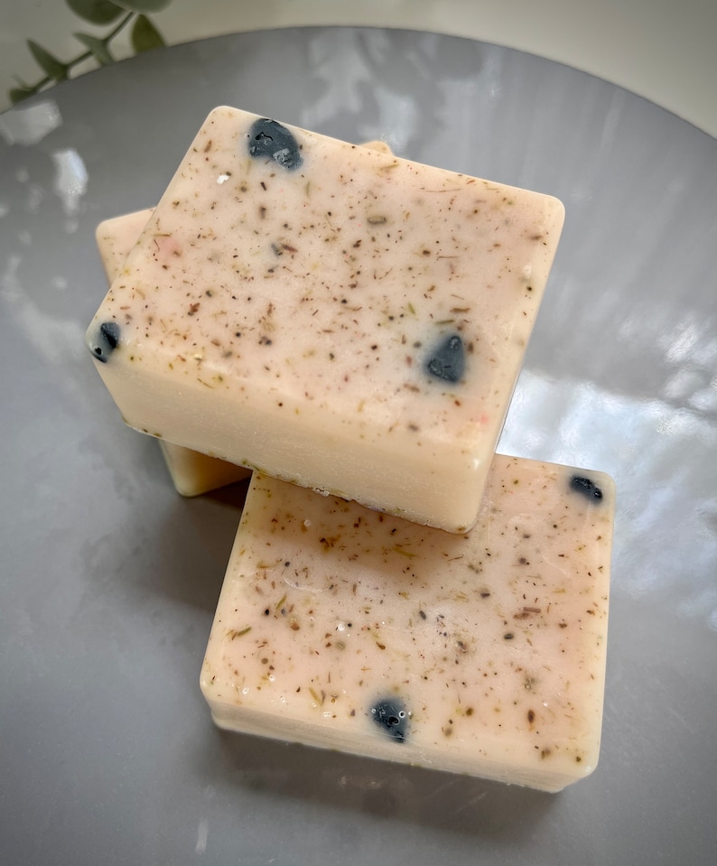 May include: Three bars of handmade soap with a light pink base and flecks of black and brown. The soap is stacked on top of each other.