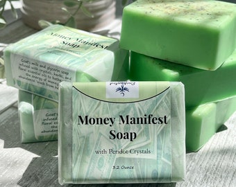 May include: Green soap bar wrapped in paper with a money design and the text "Money Manifest Soap with Peridot Crystals 3.2 Ounce".