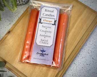 Pode incluir: Três velas rituais de cor laranja em um saco de plástico transparente com um rótulo que diz "Ritual Candles Orange Success * Creativity * Ambition * Sacral Chakra Enchanted Path MyEnchantedPath.com"