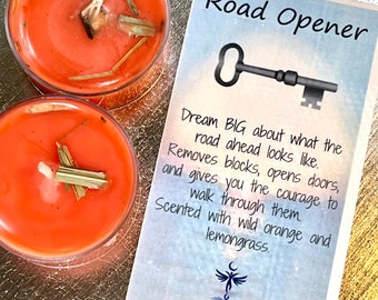 May include: Two orange scented candles with dried lemongrass inside. The card reads "Road Opener" with a key symbol and the text "Dream BIG about what the road ahead looks like. Removes blocks, opens doors, and gives you the courage to walk through them. Scented with wild orange and lemongrass."