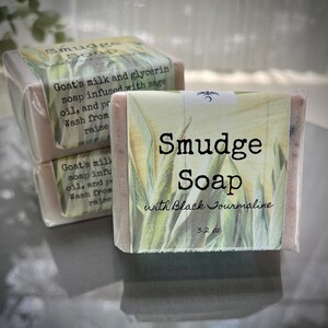 May include: Three bars of handmade soap with a green and white floral design. The label reads "Smudge Soap with Black Tourmaline 3.2 oz."