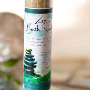 May include: A small glass jar with a silver lid filled with bath salts. The label reads "Zen Bath Soak" and includes instructions to add to your bath or foot soak for a zen experience. The label also mentions Himalayan Sea Salt and organic herbs.