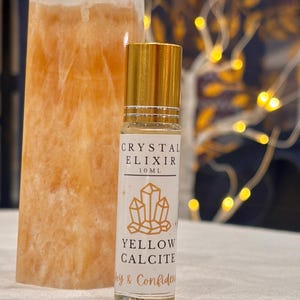 May include: A 10 ml roll-on bottle with a gold cap and label that reads "Crystal Elixir" and "Yellow Calcite". The label also features a gold illustration of crystals and the words "Joy & Confidence". A large, orange crystal is in the background.