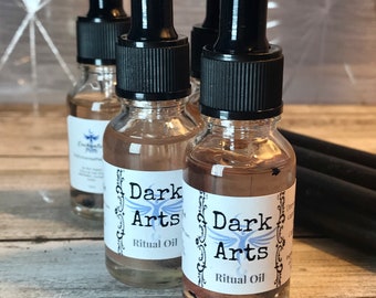 May include: Three glass bottles with black dropper tops filled with a clear liquid. Each bottle has a white label with the text "Dark Arts Ritual Oil".