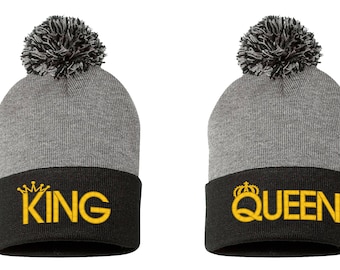 Könnte beinhalten: Zwei Strickmützen mit Bommeln. Eine Mütze ist schwarz mit einer grauen Krone und dem Wort "KING" in goldenen Buchstaben. Die andere Mütze ist schwarz mit einer grauen Krone und dem Wort "QUEEN" in goldenen Buchstaben.