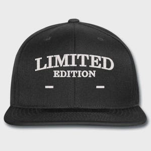 May include: A black baseball cap featuring the white embroidered text LIMITED EDITION centred on the front panel. The cap has a structured crown, a flat brim, and two small horizontal white embroidered dashes positioned below the text.