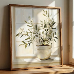 Framed olive branch wall art resting on a windowsill, softly lit by natural sunlight in a calm, neutral interior.