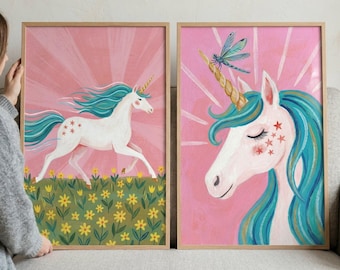May include: Two framed art prints featuring unicorns. One shows a white unicorn with blue hair running through a field of yellow flowers. The other shows a unicorn head with a dragonfly on its horn, set against a pink background.