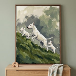 May include: A framed canvas print depicts three white Bull Terrier dogs leaping across a green, textured landscape. The artwork has a painterly style with a neutral background and a dark brown frame. The dogs are the focal point.