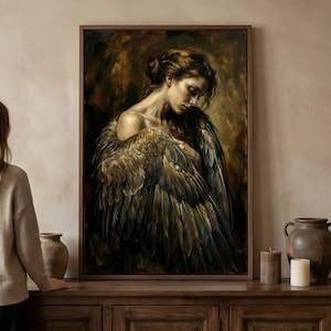 May include: A framed oil painting depicts a woman with large, feathered wings. The artwork features a warm color palette with shades of brown, gold, and touches of blue. The woman is looking down, with her wings partially wrapped around her.