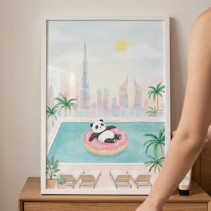 May include: A framed art print depicts a panda relaxing on a pink donut float in a pool. The pool is surrounded by palm trees and lounge chairs, with a cityscape in the background. The artwork is in a white frame.