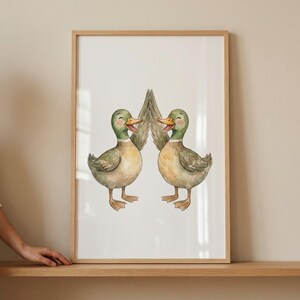 May include: Watercolour print featuring two smiling ducks with green heads, brown bodies, and orange beaks. The ducks face each other, their wings touching. The artwork is framed in a light brown wooden frame, suitable for a nursery or child's room.