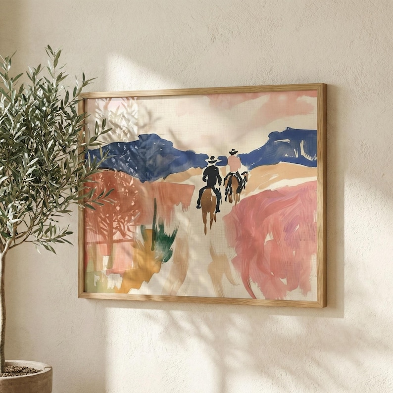 Framed abstract western wall art depicting riders on horseback in a desert landscape, softly lit by natural sunlight beside an indoor olive tree.