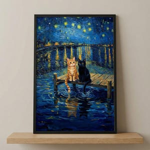 May include: Framed art print depicting two cats on a wooden dock at night. One cat is orange tabby, the other is black. The background shows a starry night sky and a body of water with reflections.