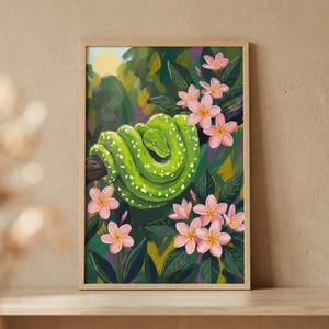 May include: A framed art print depicting a bright green snake with white spots coiled on a branch. The image is surrounded by pink flowers and green leaves, with a yellow sun in the background. The artwork is presented in a wooden frame.