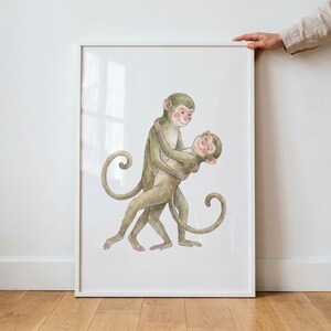 May include: A framed watercolor print featuring two embracing monkeys. The monkeys are depicted in shades of green and tan, with rosy cheeks and smiling expressions. The artwork is set against a white background, and the frame is also white.