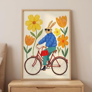 May include: A framed art print featuring a rabbit riding a red bicycle. The rabbit wears sunglasses, a blue jacket, and green pants, holding a red purse. The background includes yellow and orange flowers against a cream-colored backdrop.