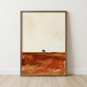 May include: A framed abstract art print depicting a rider on horseback in silhouette against a textured, earthy landscape. The artwork uses a warm palette of browns, oranges, and cream, creating a sense of the open countryside.