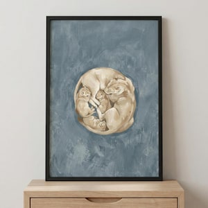 May include: Framed art print showing a lioness and cubs in a circular arrangement. The artwork depicts a mother lioness curled around her cubs, in beige and cream tones, against a muted blue-grey backdrop. The frame is black.