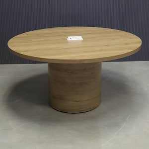 May include: A round wooden table with a light brown finish. The table has a cylindrical base and a smooth top surface.