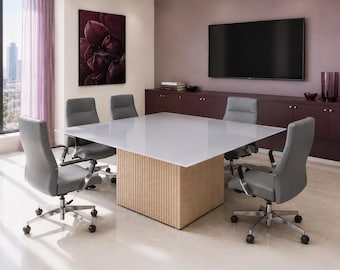 Puede incluir: Una mesa de conferencias cuadrada con superficie blanca y base de madera clara con listones, rodeada por cuatro sillas giratorias grises con reposabrazos metálicos y bases de cinco ruedas, en una oficina moderna con televisor.