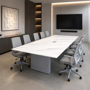 May include: A large rectangular conference table with a white marble-patterned top and a solid gray base, surrounded by ten gray mesh office chairs with wheels, positioned in a room with a wall-mounted television and a dark wood cabinet.