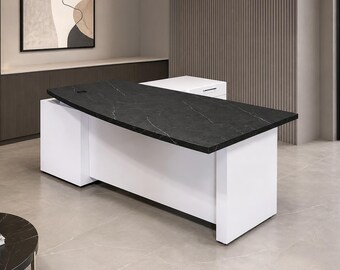 Puede incluir: Un escritorio ejecutivo moderno con un tablero rectangular negro con vetas blancas similares al mármol. El escritorio se apoya en una estructura base blanca sólida que incluye un gabinete lateral con un cajón y un tirador plateado.