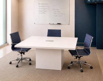 Puede incluir: Una mesa de conferencias cuadrada de color blanco con un puerto central para cables, acompañada de tres sillas de oficina de color azul marino con respaldo acanalado, marcos cromados y ruedas. Una pizarra de cristal con notas está en la pared.