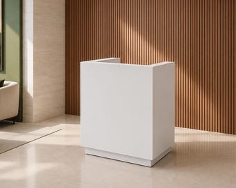 Puede incluir: Un mostrador de recepción blanco con una silueta rectangular y compacta, con un acabado liso y mate. El mueble presenta un panel frontal sólido y paneles laterales que se elevan para formar un cerramiento parcial, sobre una base retranqueada.
