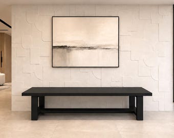 Puede incluir: Un banco negro largo y rectangular con cuatro patas robustas y una viga de soporte horizontal, colocado debajo de un gran cuadro de paisaje enmarcado que presenta capas horizontales abstractas en tonos beige, crema y gris oscuro.