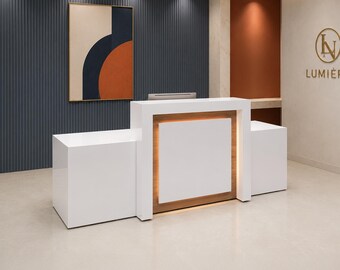 Puede incluir: Un mostrador de recepción blanco con un panel central elevado e iluminación cálida integrada, con un diseño elegante de varios niveles. El mostrador se sitúa en una estancia con una pared azul oscuro acanalada, arte abstracto y un logotipo dorado.