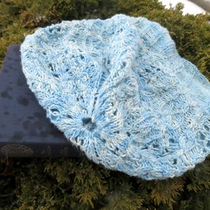 A fingering-weight cable and lace beanie hat laying flat. The hat has a lengthy ribbed rib that flows into intricate cables and lace.