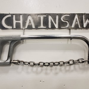 May include: A silver metal saw with a chain and a handle. The saw is hanging on a metal sign that says "Chainsaw".