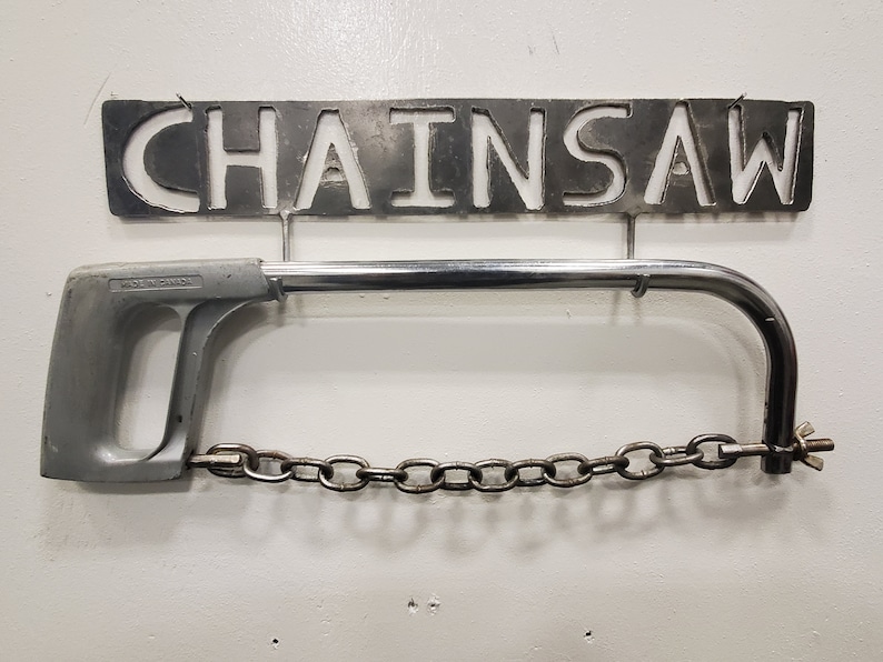 May include: A silver metal saw with a chain and a handle. The saw is hanging on a metal sign that says "Chainsaw".