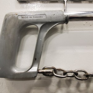 May include: A silver hand saw with a chain attached to the end. The saw handle has the text "MADE IN CANADA" printed on it.
