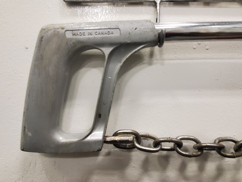 May include: A silver hand saw with a chain attached to the end. The saw handle has the text "MADE IN CANADA" printed on it.