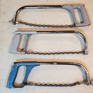 May include: Three hand saws with chains. The top saw is silver with a black chain. The middle saw is silver with a black chain. The bottom saw is blue with a silver chain.