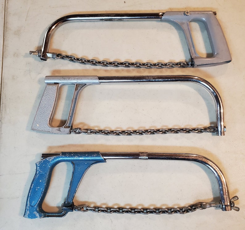 May include: Three hand saws with chains. The top saw is silver with a black chain. The middle saw is silver with a black chain. The bottom saw is blue with a silver chain.