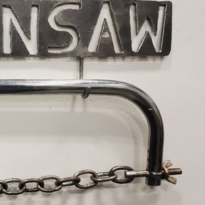 May include: A metal saw holder with a chain and a metal sign that says "SAW" hanging above it.