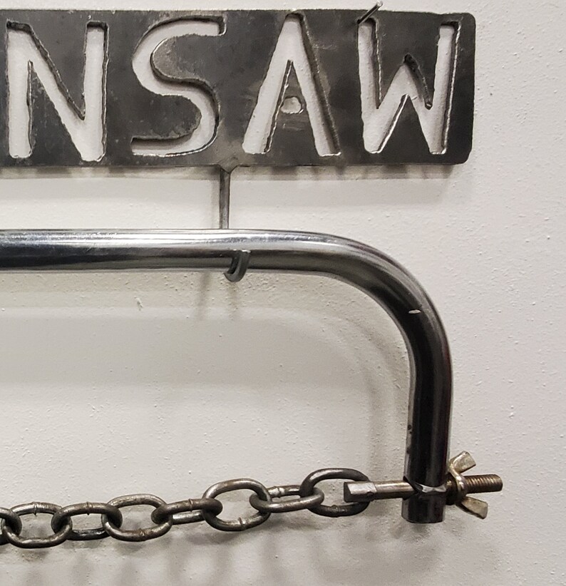 May include: A metal saw holder with a chain and a metal sign that says "SAW" hanging above it.