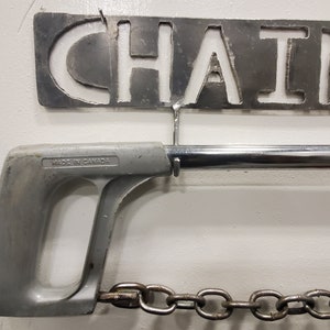 May include: A silver metal saw with a gray plastic handle and a chain attached to the end. The saw is labeled "Made in Canada".